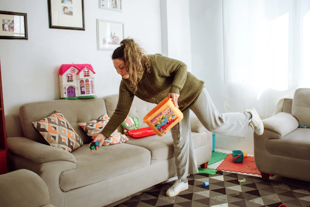 A friendly cleaner smiling while tidying a bright, modern living room.