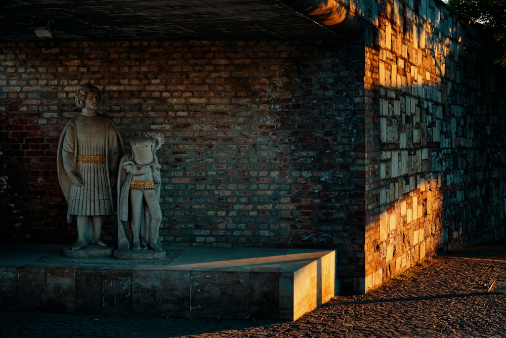 a statue of a man and a woman standing in front of a brick wall