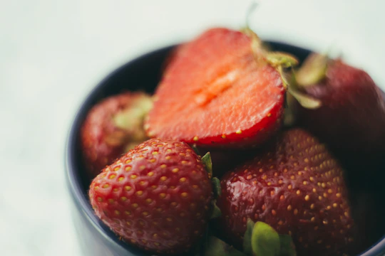 Close-up of vibrant frozen strawberries and mango chunks in a rustic wooden bowl.