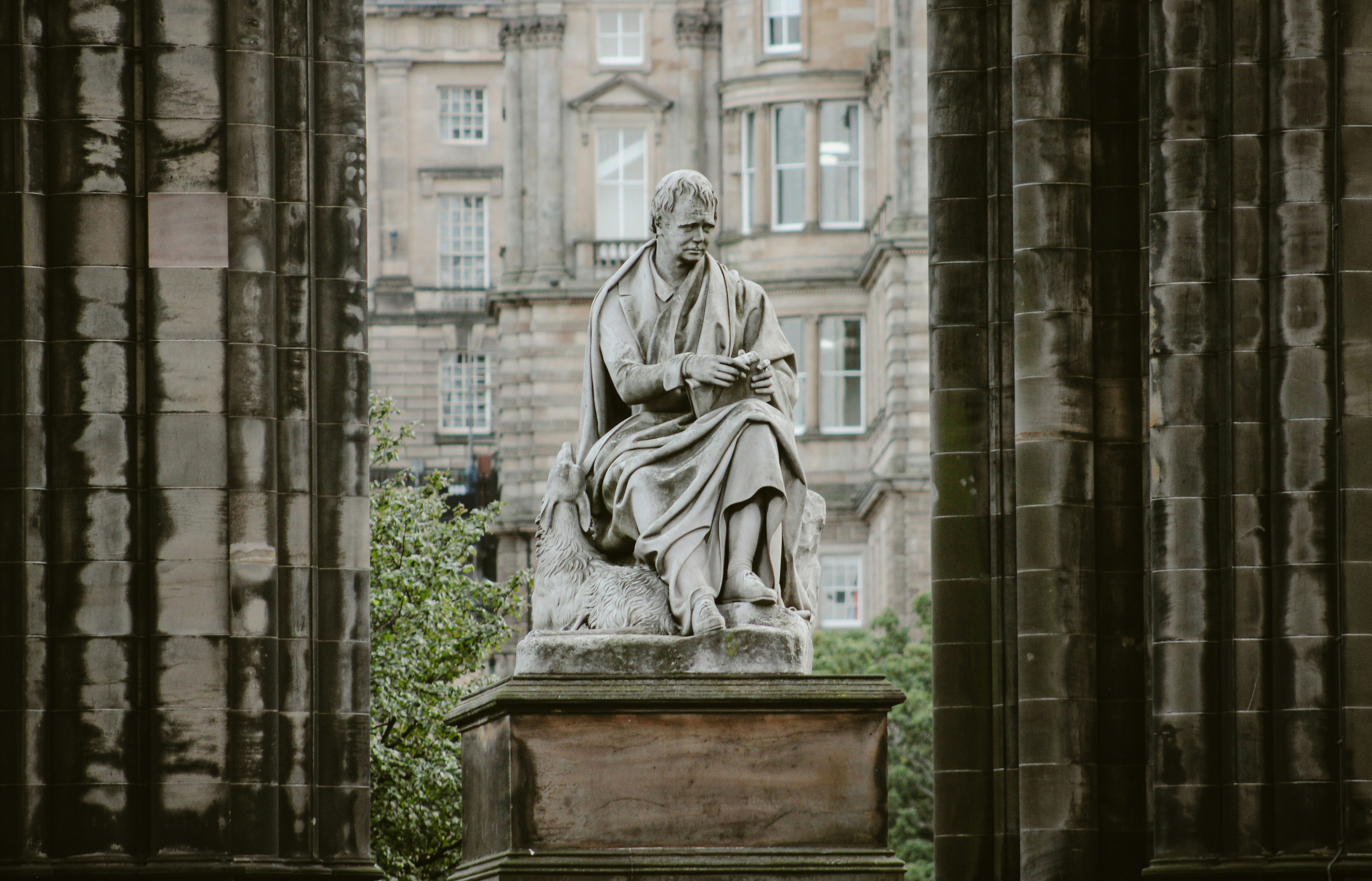 a statue of a person sitting on a stone pedestal in front of a building, 