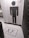 The image depicts a bathroom entrance with a tile design featuring a large, stylized person icon made from black hexagonal tiles against a white hexagonal tile background. The floor also consists of white hexagonal tiles with a black 'XX' symbol inside a rectangular border near the entrance. A trash can is visible on the left side.