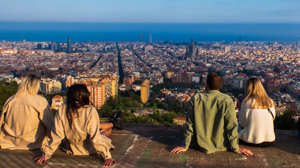 a group of people sitting on a ledge overlooking a city