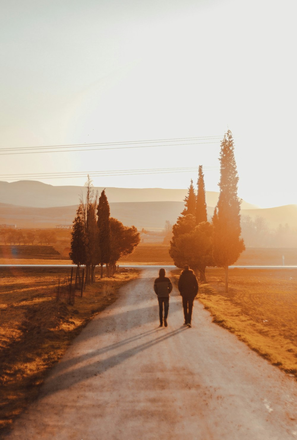 a man and woman walking down a dirt road with trees on either side