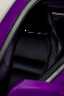 A close-up view of a black leather car seat, with purple accents visible around the edges. The seat features a textured and perforated design, suggesting comfort and style. The image focuses on the sleek and modern design elements of the car's interior.