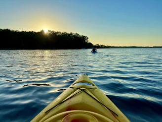A serene kayak gliding on calm estuary waters at sunrise with soft golden light.