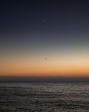 A sleek futuristic cargo plane soaring over a dark blue ocean at dusk