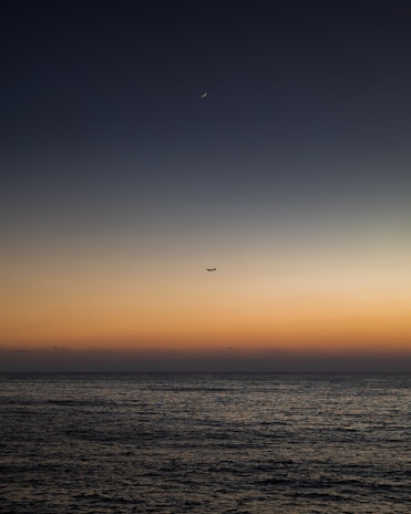 A sleek futuristic cargo plane soaring over a dark blue ocean at dusk