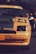 A close-up view of the front portion of an orange Renault car displaying the number 94. The car is parked outdoors, with some people visible in the background. The lighting suggests late afternoon or early evening, creating a subtle contrast between the car and the darker surroundings.