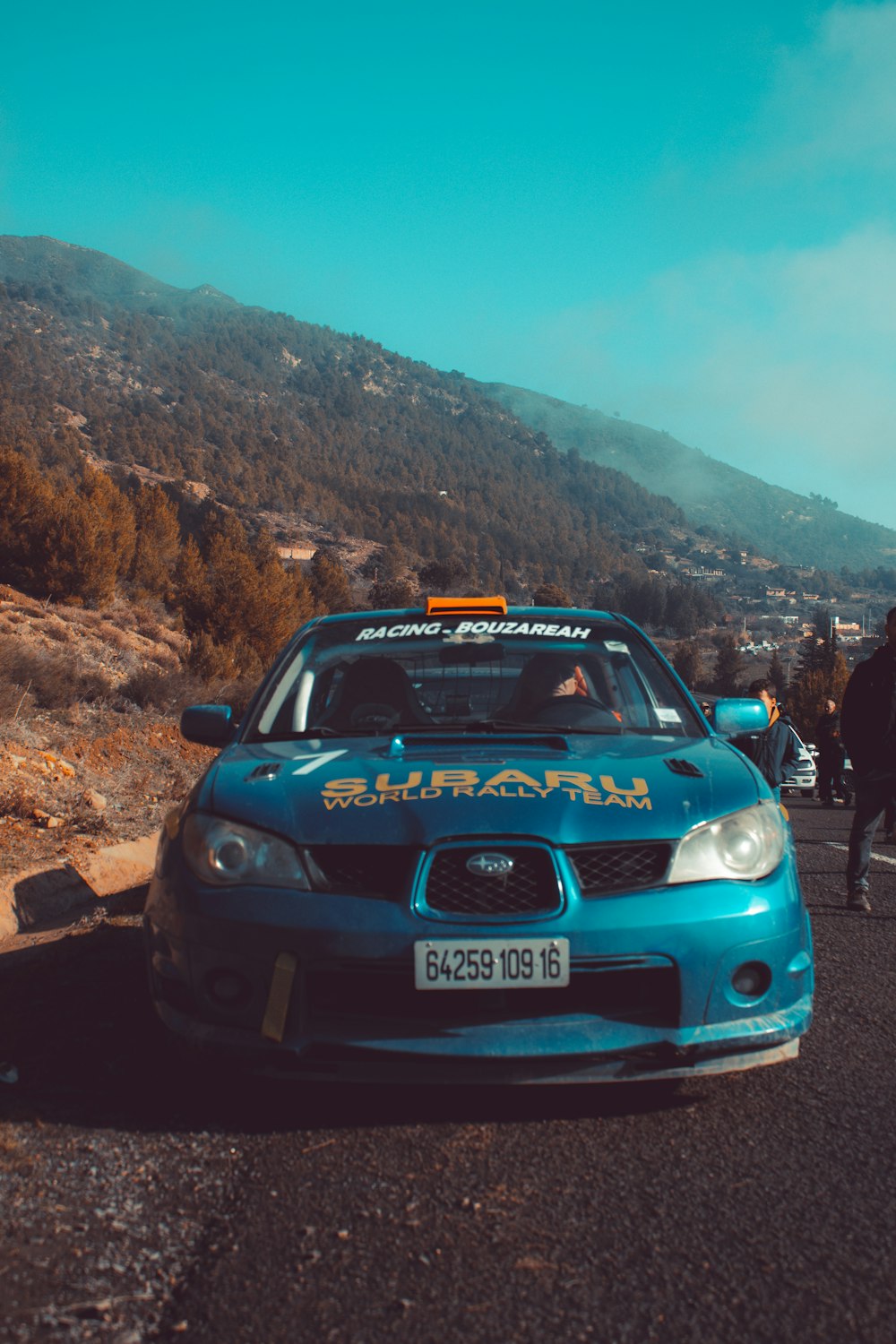 a blue car on a road with a mountain in the background
