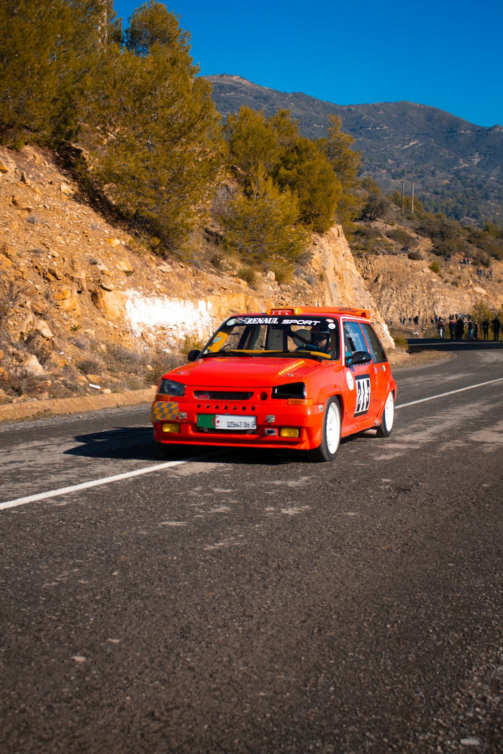 a red car on a road with trees and mountains in the background