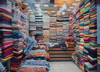 a couple of men sitting on a bed with a large pile of colorful fabric