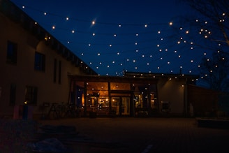 Night view of a barndominium lit warmly with outdoor string lights and a welcoming porch.