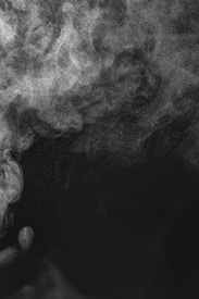 A swirling formation of white smoke or mist against a dark background, creating an ethereal and mysterious atmosphere. The texture appears soft and diffuse, giving a sense of movement and fluidity.