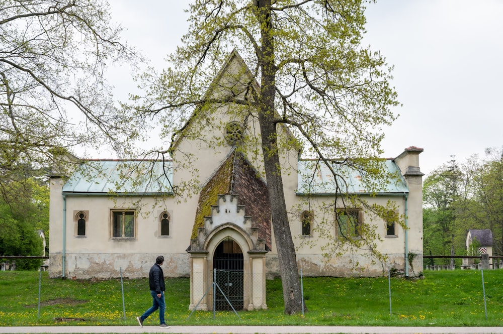 a person walking in front of a white building with a large tree in front