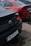 Two parked cars with different color schemes, one black and one red, possibly BMW models, are seen from their rear ends. Both cars have visible license plates, with the black car showing 'TO-777-RT' and the red car showing 'MZ-2022-01'. The ground has patches of water, indicating recent rain, and the cars appear to have water droplets on their surfaces.