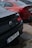 Two parked cars with different color schemes, one black and one red, possibly BMW models, are seen from their rear ends. Both cars have visible license plates, with the black car showing 'TO-777-RT' and the red car showing 'MZ-2022-01'. The ground has patches of water, indicating recent rain, and the cars appear to have water droplets on their surfaces.