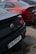 Two parked cars with different color schemes, one black and one red, possibly BMW models, are seen from their rear ends. Both cars have visible license plates, with the black car showing 'TO-777-RT' and the red car showing 'MZ-2022-01'. The ground has patches of water, indicating recent rain, and the cars appear to have water droplets on their surfaces.