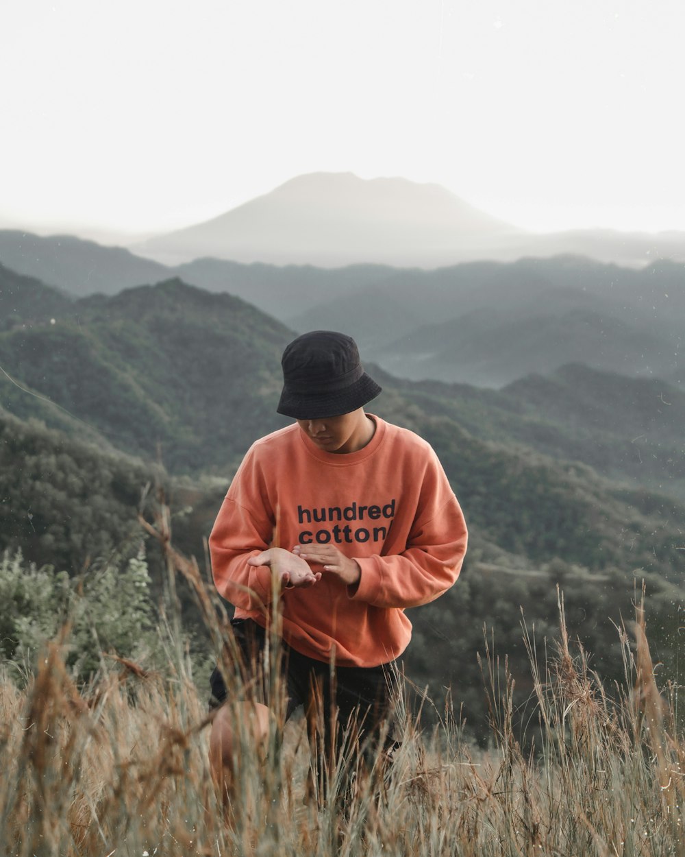 a man in a hat standing on a hill with a mountain in the background