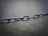 A close-up of a metal chain with multiple links connected, captured in a shallow depth of field. The background is blurred, emphasizing the chain's detail and metallic texture.