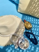 A stylish straw hat with a subtle bow, placed beside a woven beach bag and sunglasses on a sunlit deck.