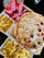A meal spread featuring a large pizza topped with cheese, onions, and various meats. Surrounding the pizza are several boxes of golden, crispy French fries. Three cans of Coca-Cola Classic are placed nearby, along with a stack of ketchup sachets.