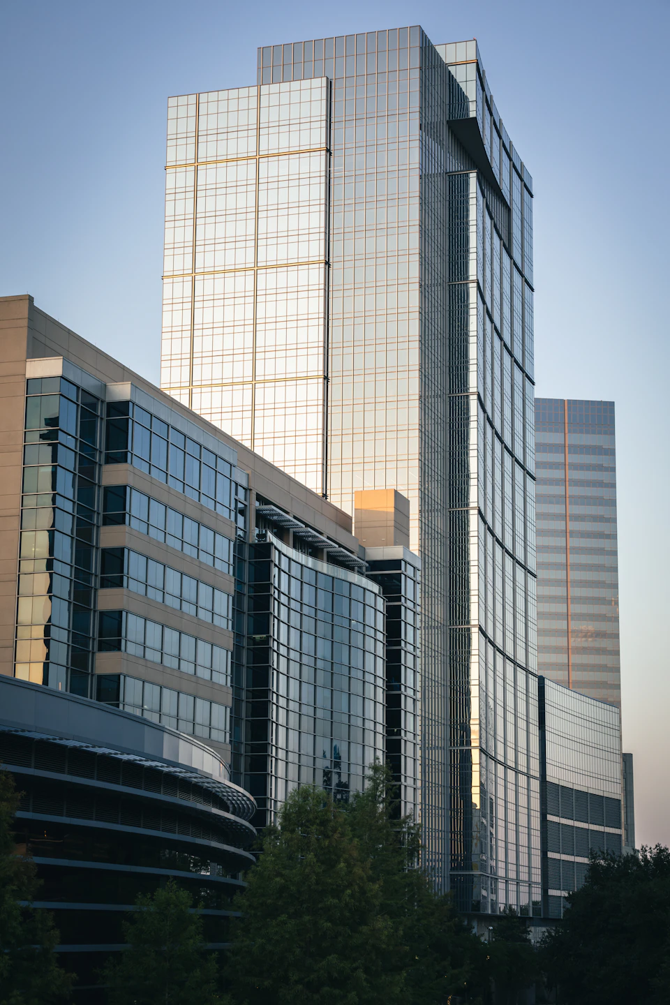 Three tall buildings with distinct architectural styles and colors in a clear blue sky