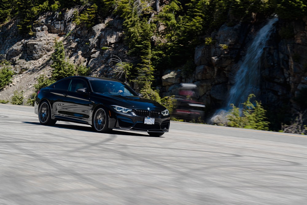 a black car on a road with a waterfall and trees