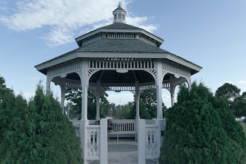 Elegant wooden gazebo with detailed carvings in a sunny park.