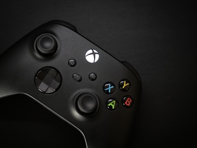 A black gaming controller with colorful buttons labeled X, Y, A, and B. The controller has a sleek design with two analog sticks and a directional pad.