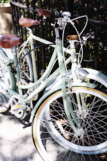 A vintage cruiser bike resting against a weathered fence with a steaming mug balanced on the seat.