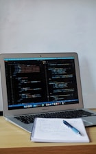 a laptop with a pen and paper on the table