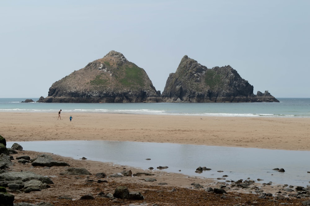 a beach with a few people and large rocks in the distance with Haystack Rock in the background