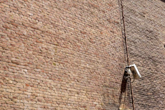 Technician installing electronic security devices on a building wall.