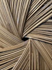 Close-up of an intricate woven pattern made from natural materials, possibly bamboo or rattan, featuring a radial design with overlapping strips.