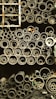 A collection of pipes stored in an organized manner, ranging from large to small diameters. The pipes are stacked vertically and closely packed, giving a sense of industrial storage. A metal ladder is positioned on the left side, partially visible.