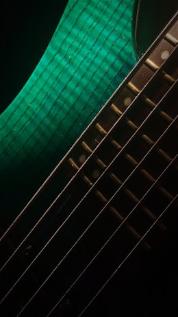 A close-up view of a guitar, focusing on its shiny metallic strings and vibrant green body with a textured pattern.