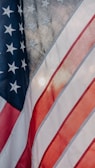 The image features the American flag with portions of its stars and stripes visible. The blue field displays white stars, and the red and white stripes are shown in a flowing motion, indicating movement or wind.