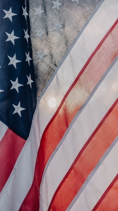 The image features the American flag with portions of its stars and stripes visible. The blue field displays white stars, and the red and white stripes are shown in a flowing motion, indicating movement or wind.