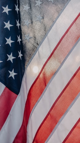 The image features the American flag with portions of its stars and stripes visible. The blue field displays white stars, and the red and white stripes are shown in a flowing motion, indicating movement or wind.