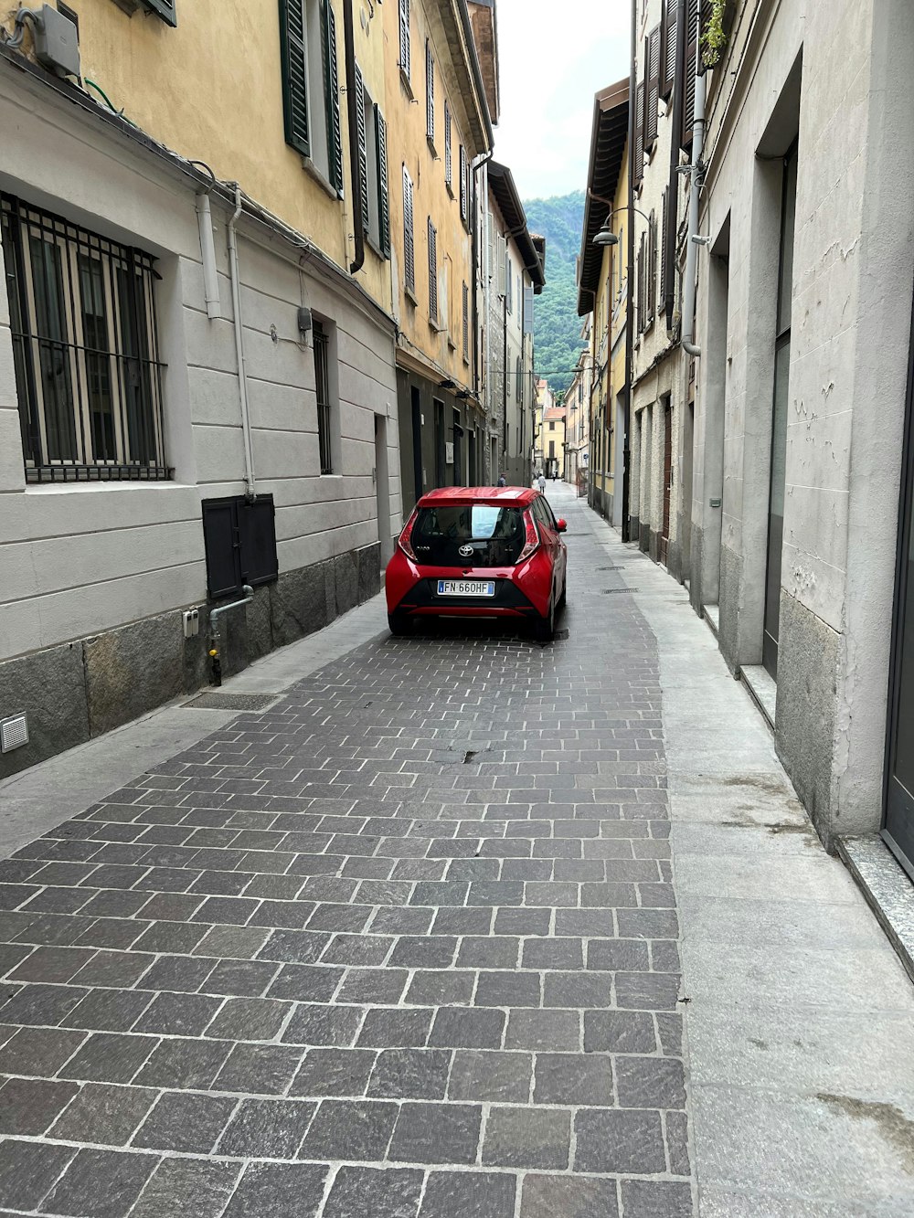 Un coche rojo aparcado en una calle empedrada entre edificios