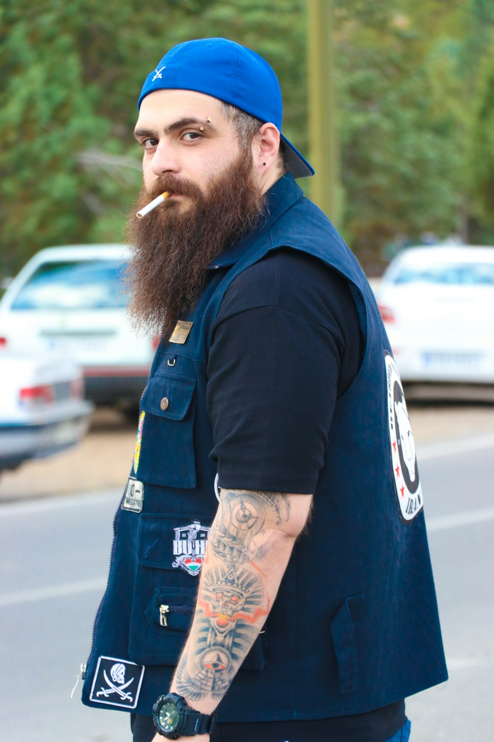 a man with a beard and a blue hat smoking a cigarette