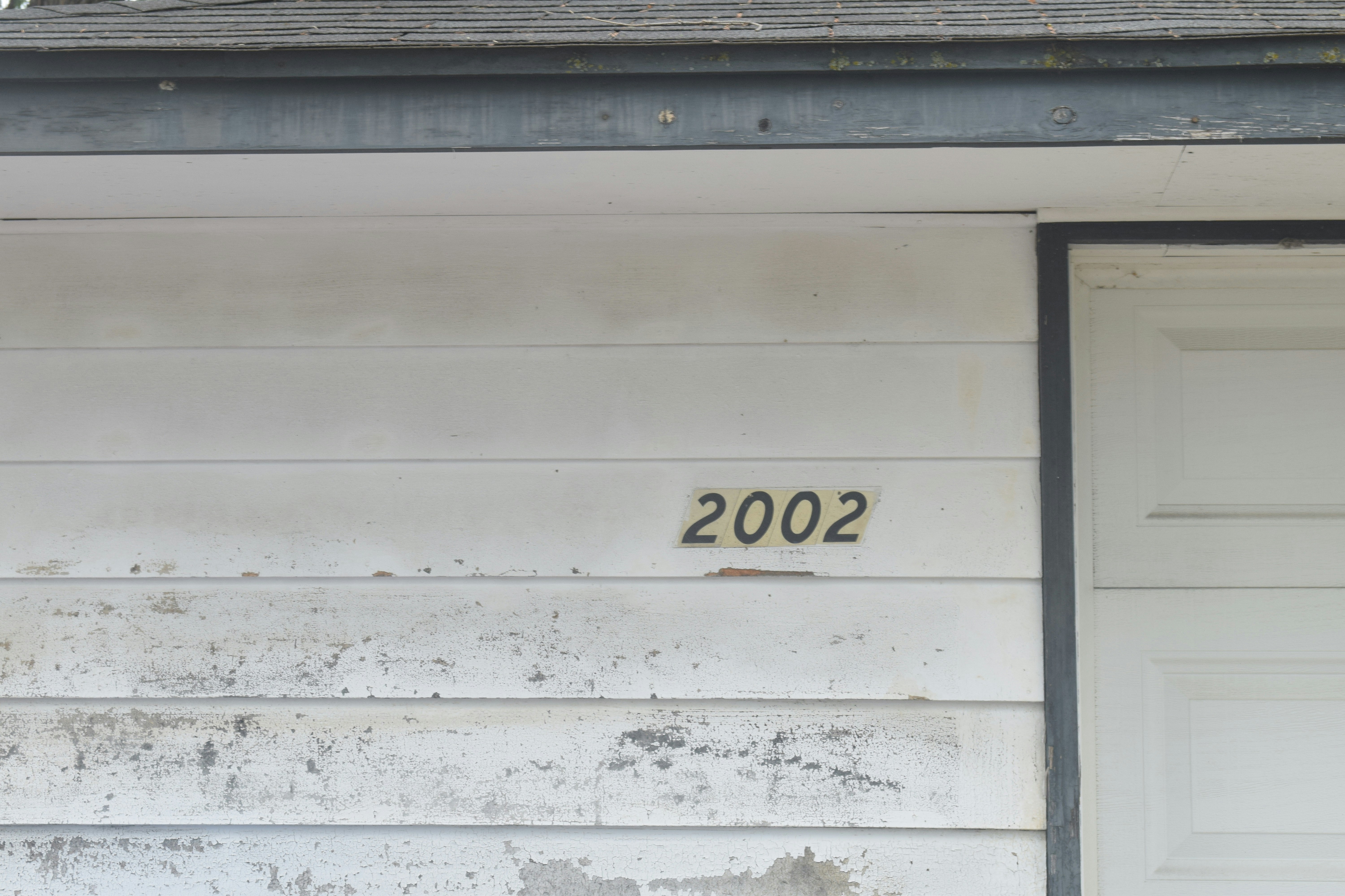 Black house numbers stenciled on weathered white siding.