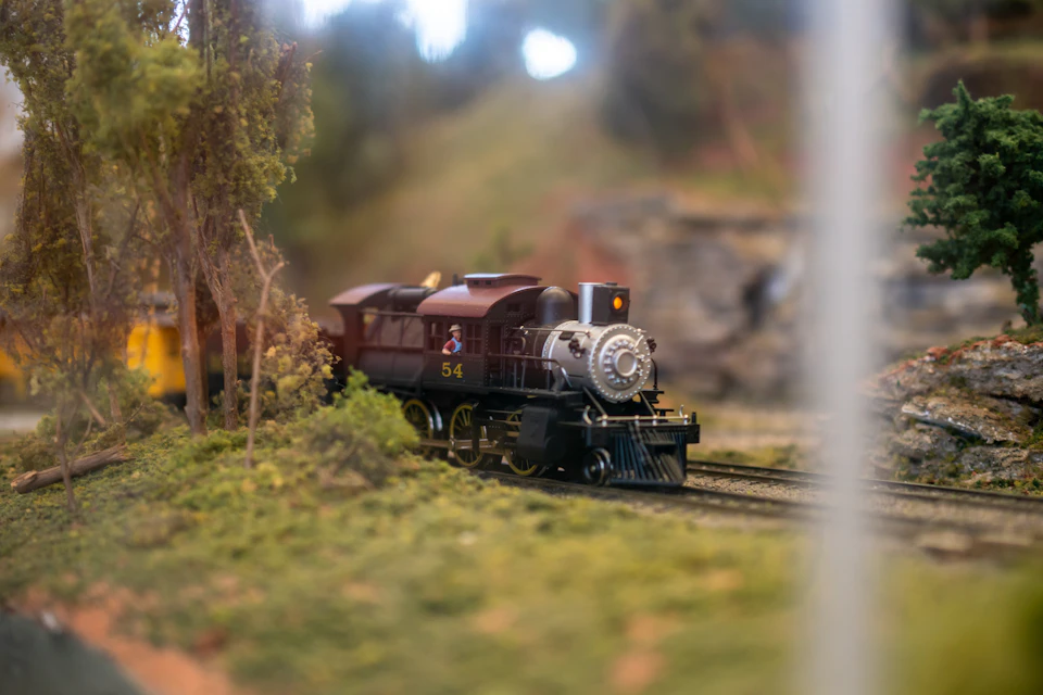 Miniature red and black train engine pulls small passenger car along a track in landscape