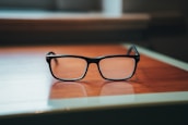 A close-up of prescription glasses on a wooden table.