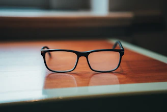 Close-up of stylish eyeglasses resting on a wooden table with soft lighting.