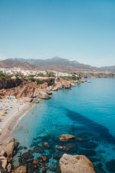 a beach with rocks and a body of water with a town in the distance