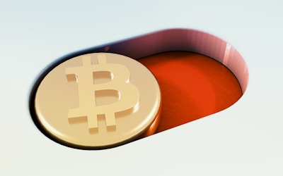 A gold coin embossed with the Bitcoin symbol is placed inside a red, pill-shaped recess. The background includes soft gradients of light colors, contrasting with the coin's golden hue.