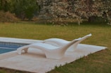 Close-up of plush designer pillows in muted tones arranged on an elegant outdoor lounge chair by a pool.