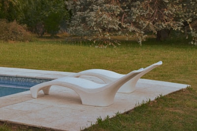 Close-up of plush designer pillows in muted tones arranged on an elegant outdoor lounge chair by a pool.