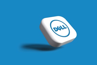A white, cube-shaped key with a blue circular logo on its front appears to be floating above a blue background. The logo features a slightly tilted word in blue with a shadow beneath the key, giving an impression of depth.